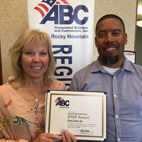 Two people smiling indoors, holding a STEP Award certificate from Associated Builders and Contractors, Rocky Mountain Region. A banner is partially visible in the background.